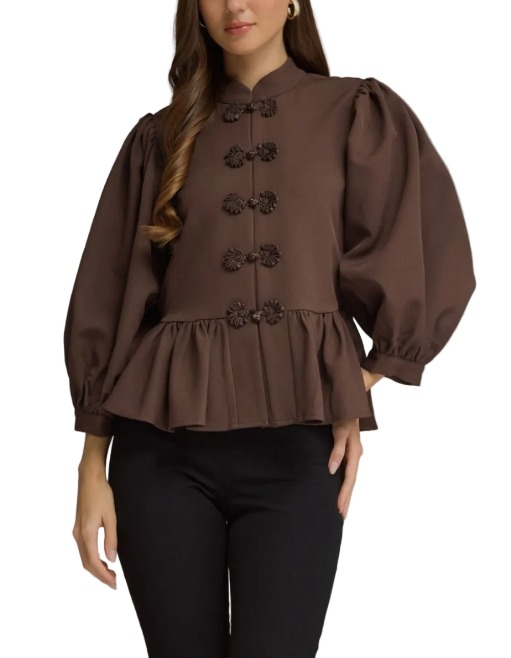 A woman modeling a brown long-sleeve blouse with puff sleeves, a high collar, and decorative button details down the front, paired with black pants against a neutral gray studio background.