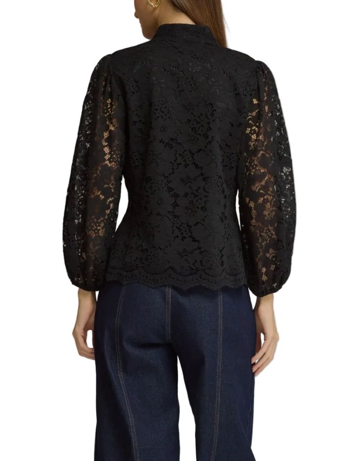 A woman shown from the back wearing a black lace long-sleeve blouse with sheer lace sleeves and dark blue jeans, photographed against a plain gray studio background.