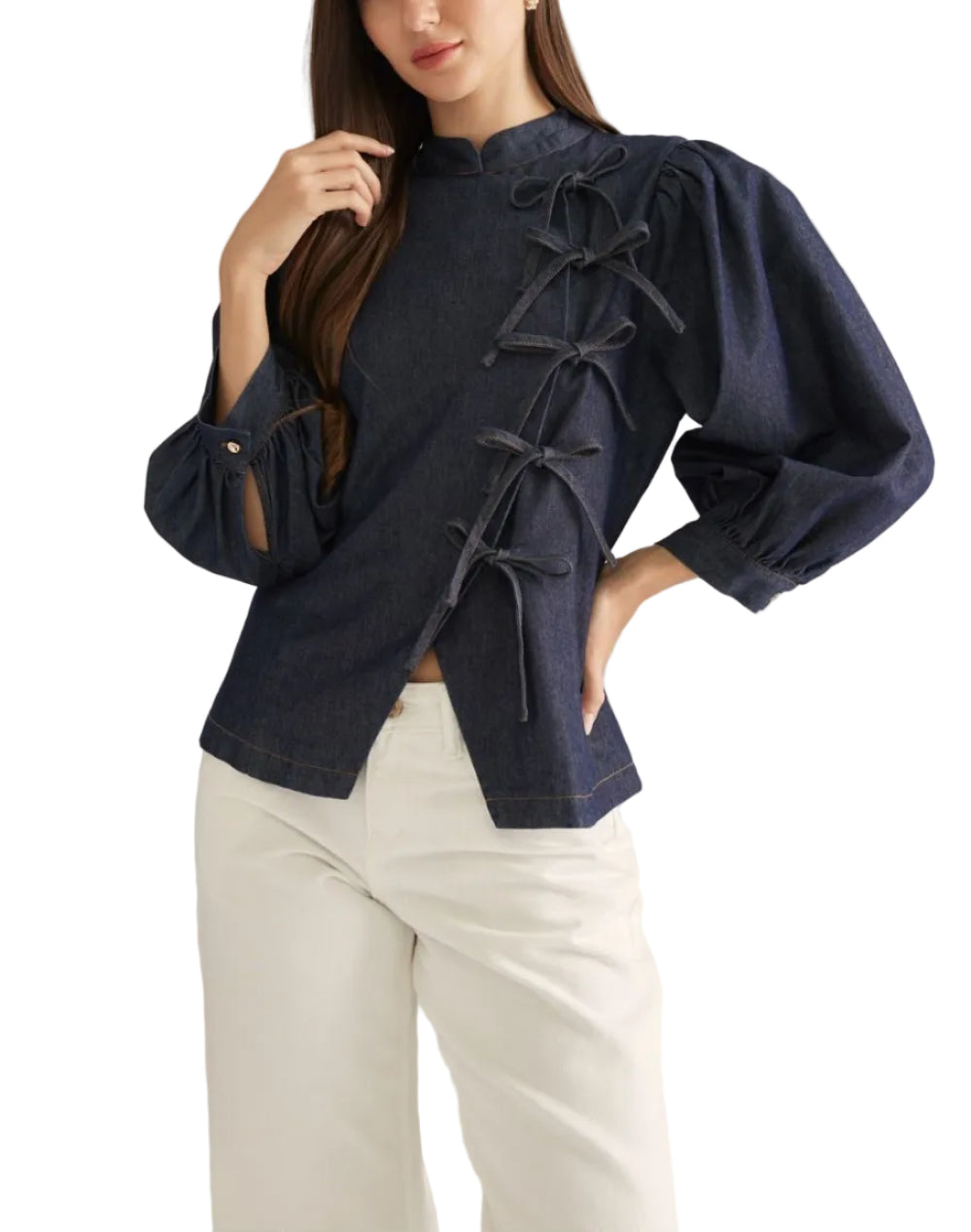 A woman modeling a navy blue cropped jacket with dramatic puffed sleeves and front tie details, paired with white pants, against a plain light gray studio background.