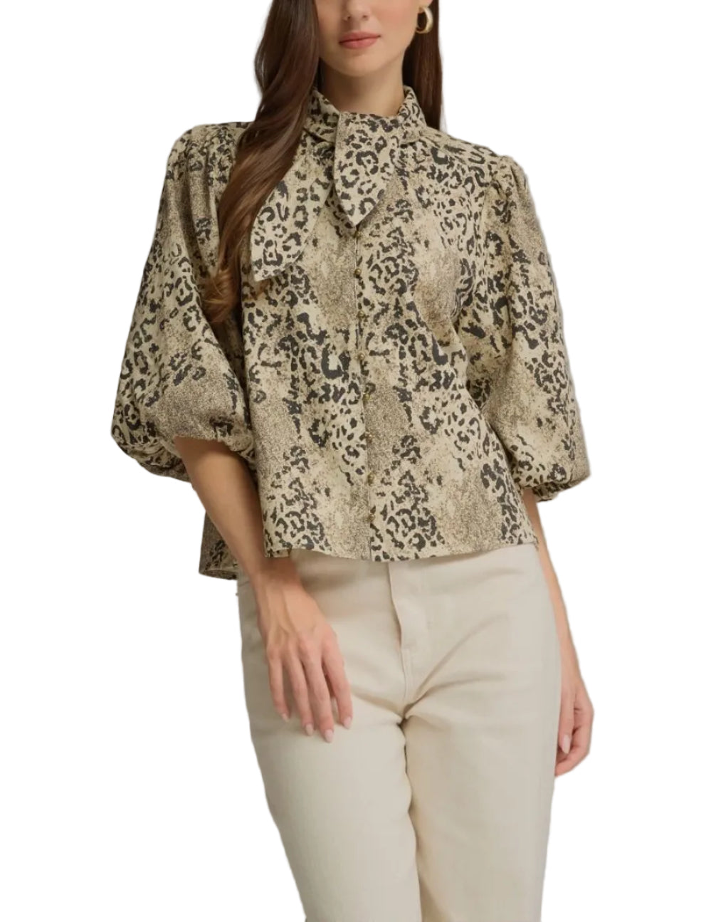 A woman modeling a beige and black leopard-print blouse with puff sleeves and a high collar, paired with cream-colored pants, against a solid gray studio background.
