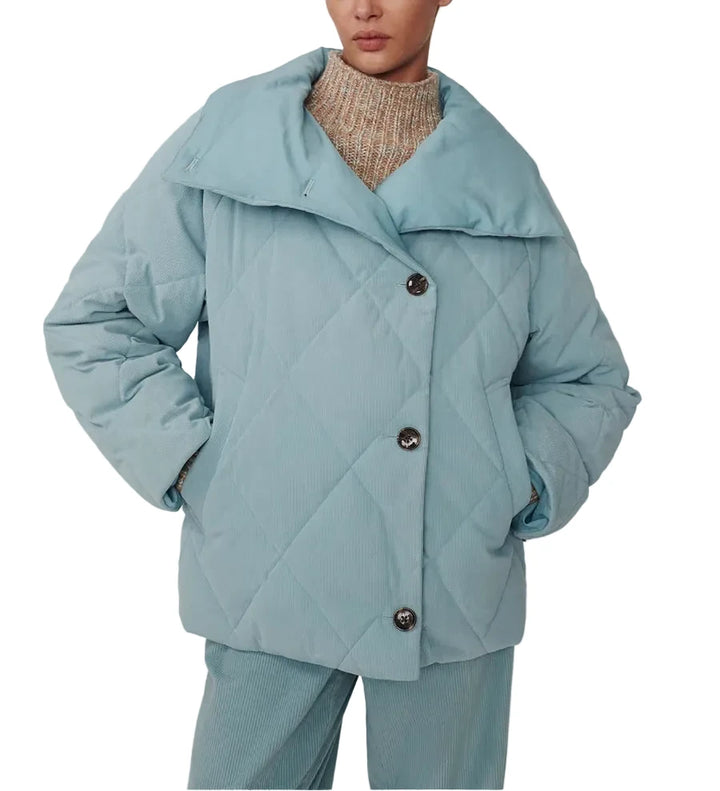 A model wearing a light blue quilted puffer jacket with a wide collar and dark buttons, paired with matching light blue trousers and a beige knit turtleneck, against a plain light gray background.