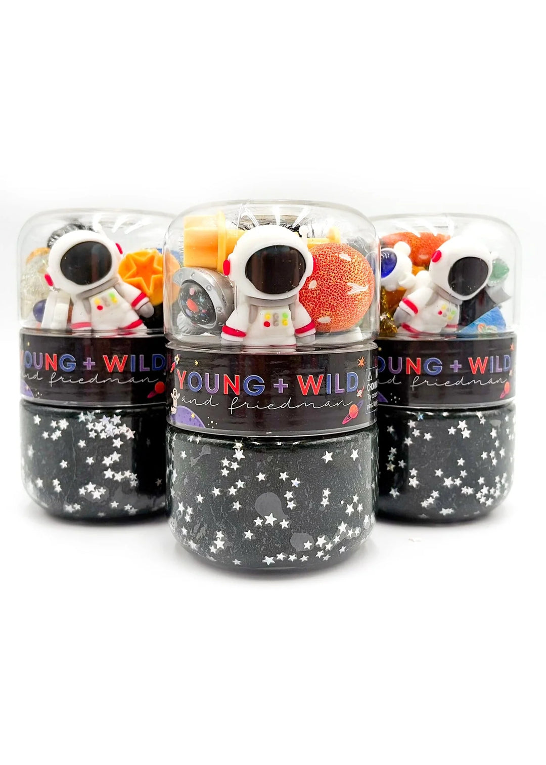 Three small cylindrical containers with clear domes and black starry bases, each containing colorful astronaut-shaped items, photographed on a white background.