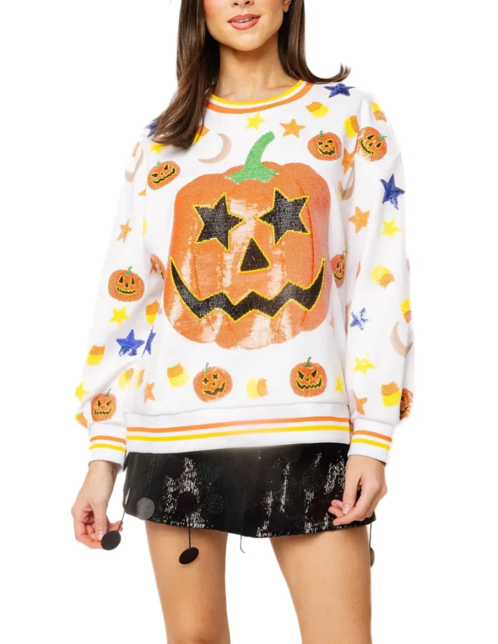A woman modeling a white long-sleeve crewneck sweater with a large orange jack-o'-lantern graphic on the front, surrounded by smaller pumpkins, stars, and moons, paired with a black mini skirt against a plain white background.