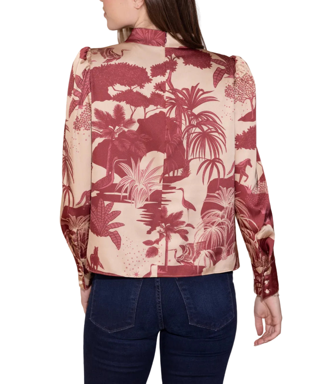 A woman shown from the back wearing a long-sleeve collared jacket with a tropical palm leaf pattern in deep red and beige, paired with dark blue jeans, against a solid beige background.