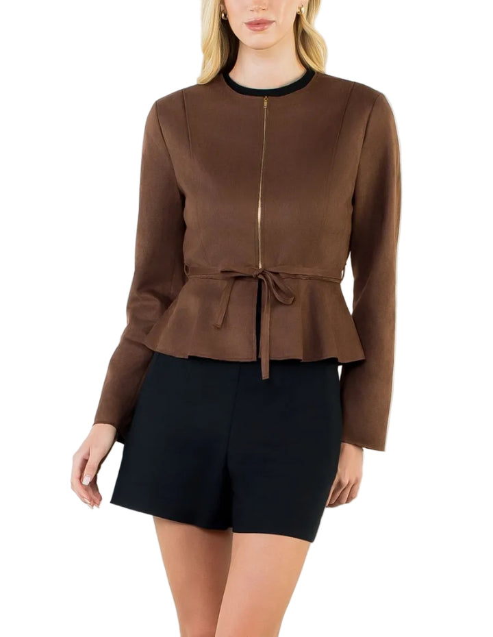 A woman modeling a brown long-sleeve cropped jacket with a front zipper, peplum waist tie, and black shorts against a plain white studio background.