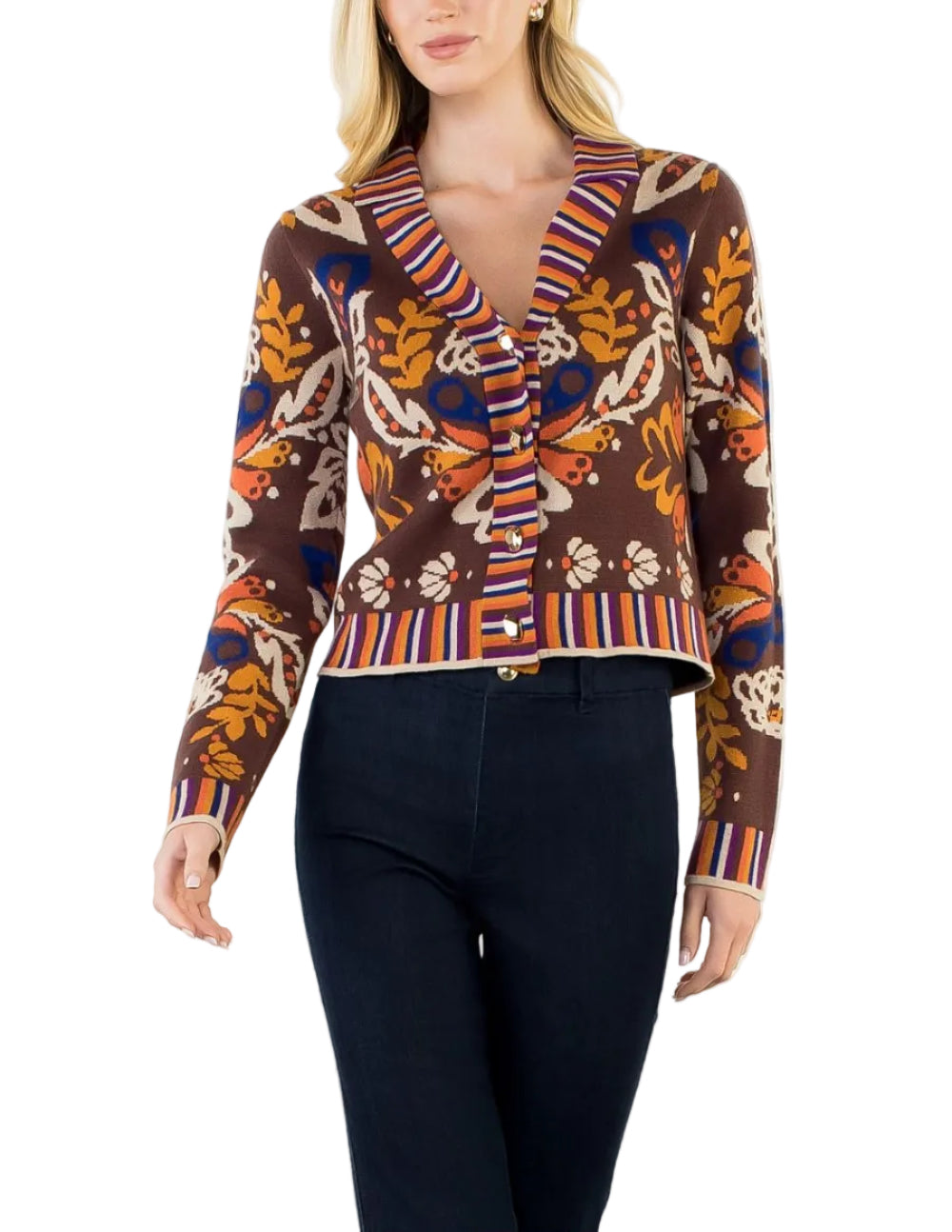 A woman modeling a brown knit cardigan with a colorful abstract pattern and striped trim, paired with dark navy pants, against a plain white background.